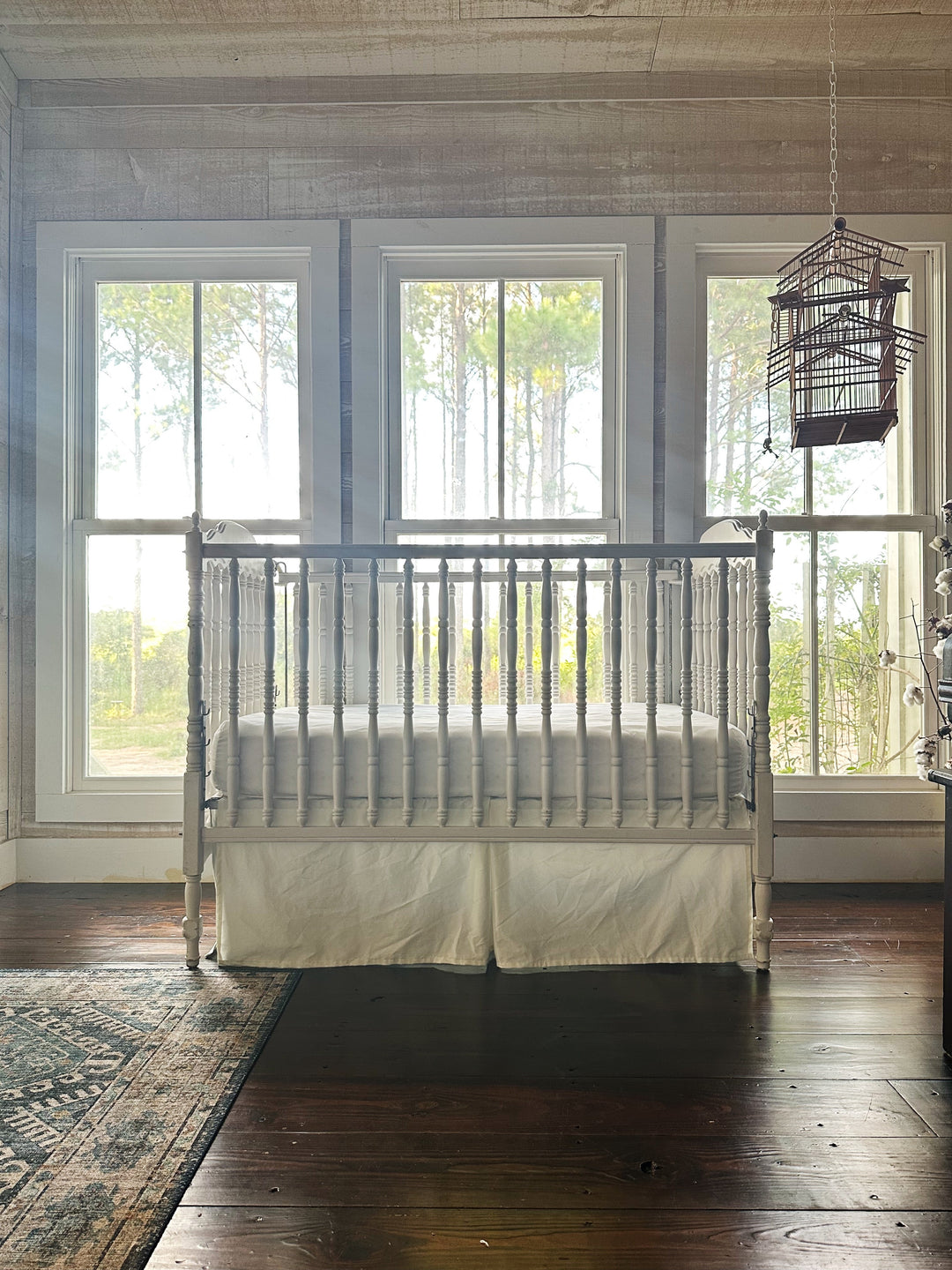 Farmhouse nursery with shiplap walls, dark pine floors and a spindle crib dressed in a porcelain tailored crib skirt - High Cotton Textile