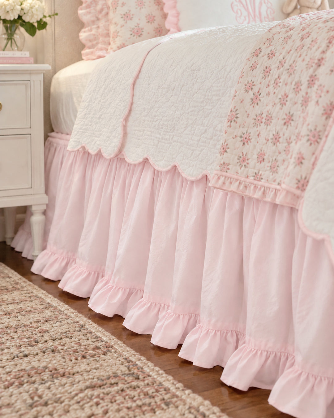 Close up of the gathered baby pink twin bed skirt and its ruffled hem beside a white nightstand - High Cotton Textile