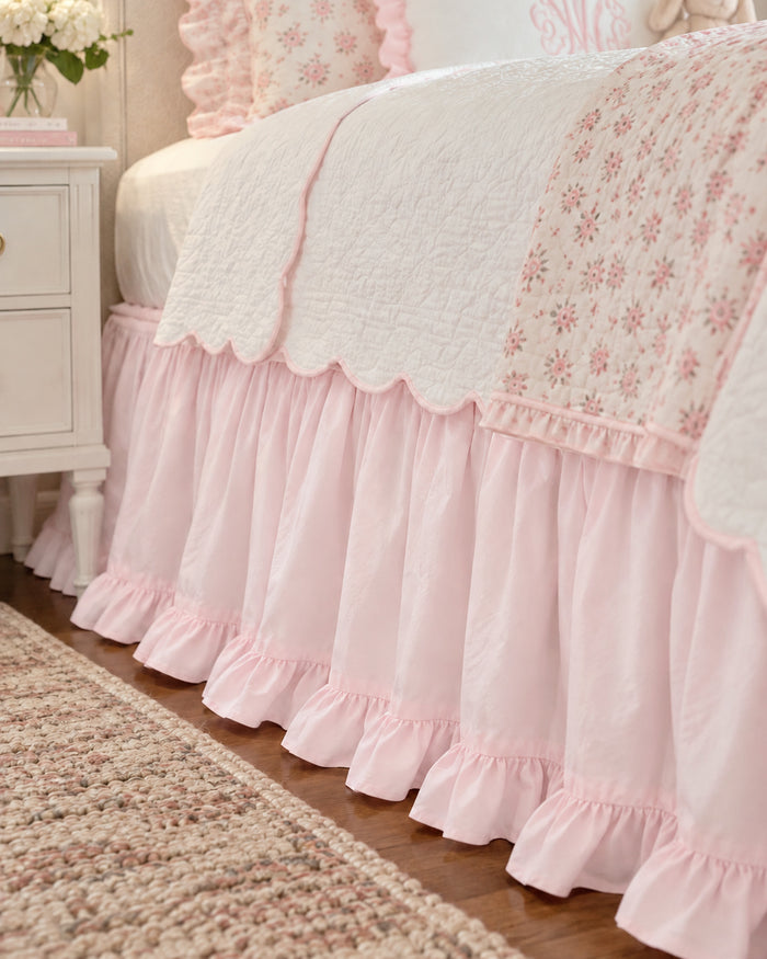 Close up of the gathered baby pink twin bed skirt and its ruffled hem beside a white nightstand - High Cotton Textile