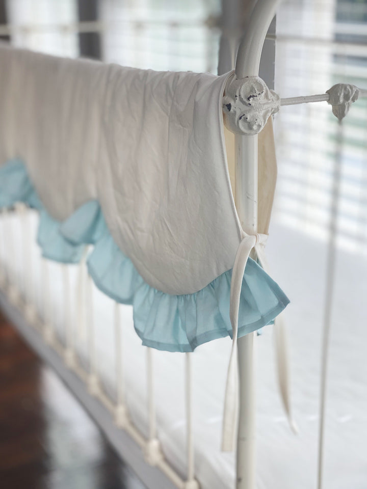 Side view of the ivory crib rail cover draping over an iron crib rail with a mist ruffle