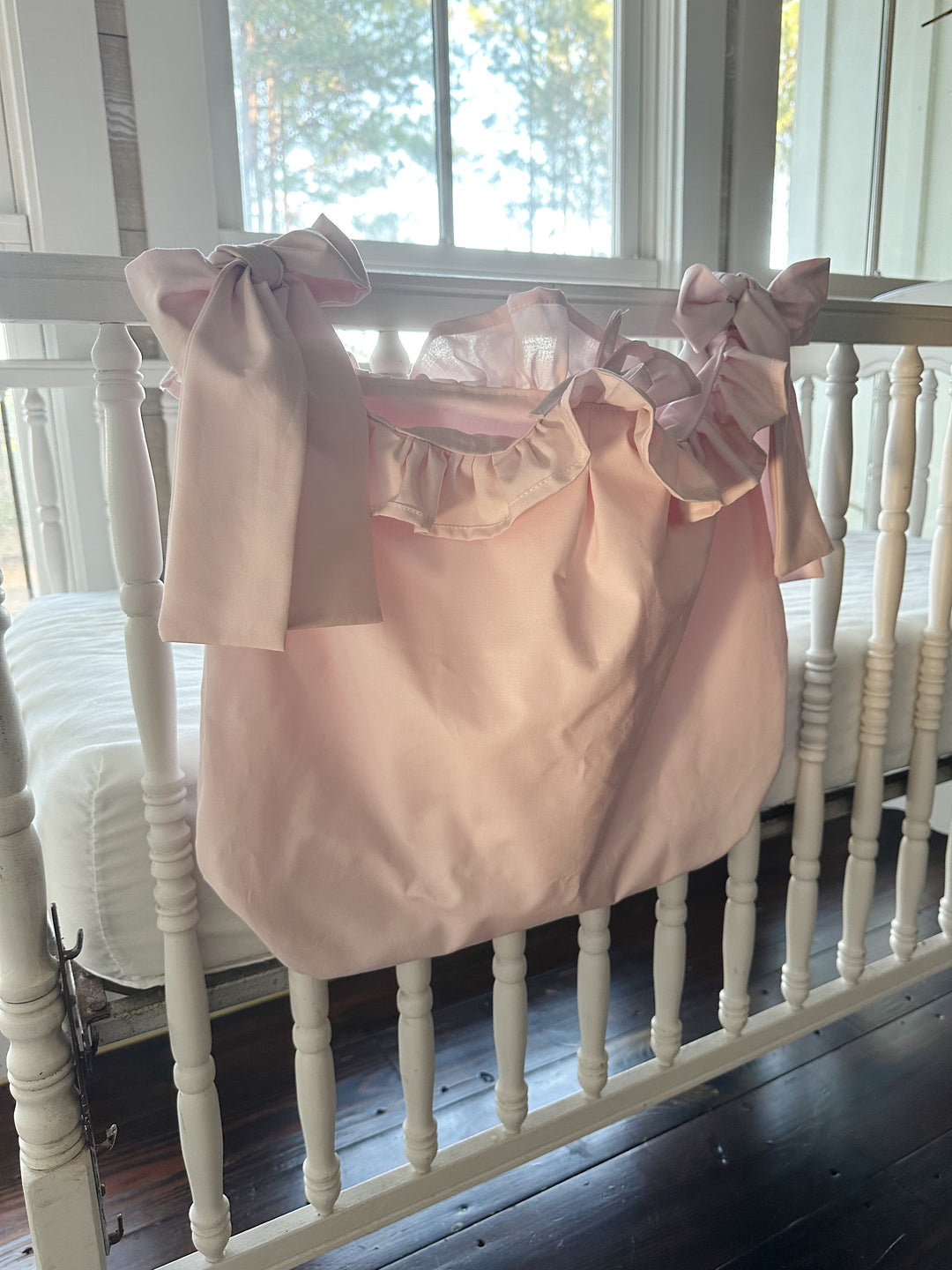 Angled view of the pink caddy on the crib rail, the ruffle framing the open top
