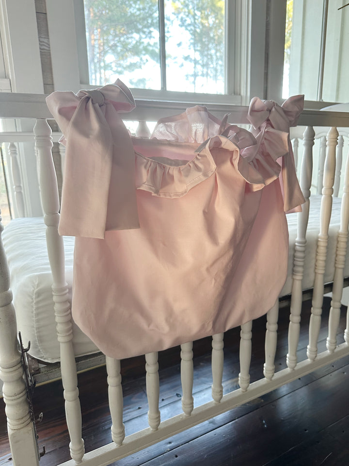 Angled view of the pink caddy on the crib rail, the ruffle framing the open top