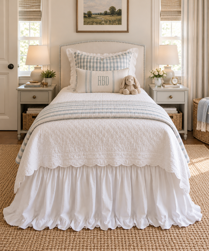 Straight on view from the foot of a twin bed showing the white ruffled bed skirt below a scalloped coverlet - High Cotton Textile