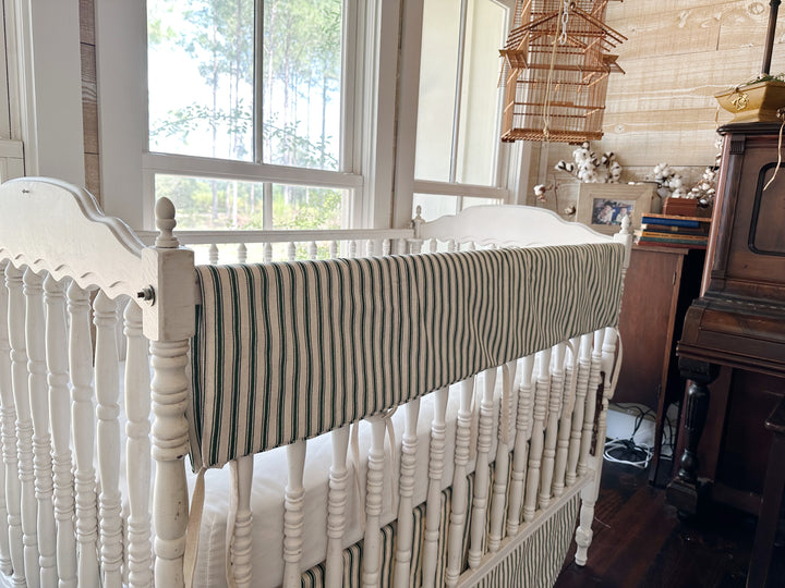 Angled view down the crib rail with the ticking cover folded over it and the striped skirt below