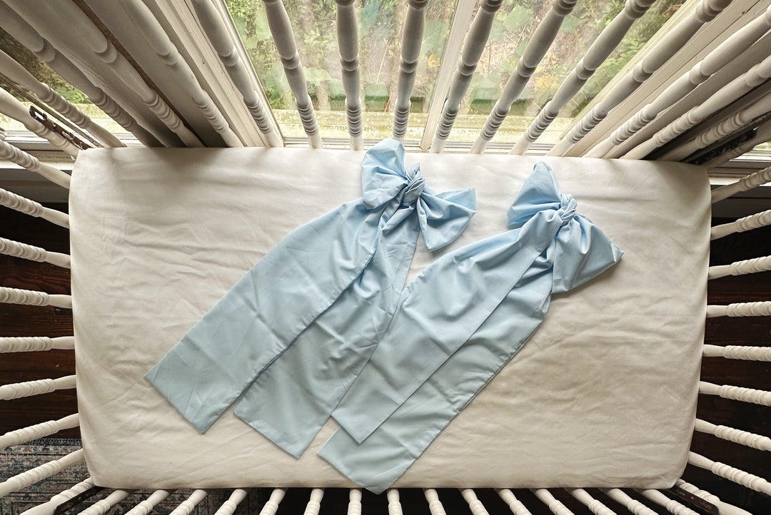 Two heirloom blue crib bows laid flat on the crib mattress showing the long sash form