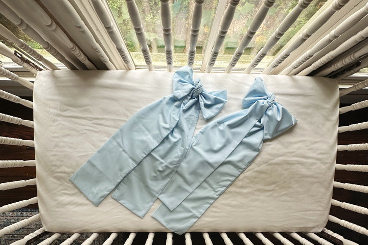 Two heirloom blue crib bows laid flat on the crib mattress showing the long sash form