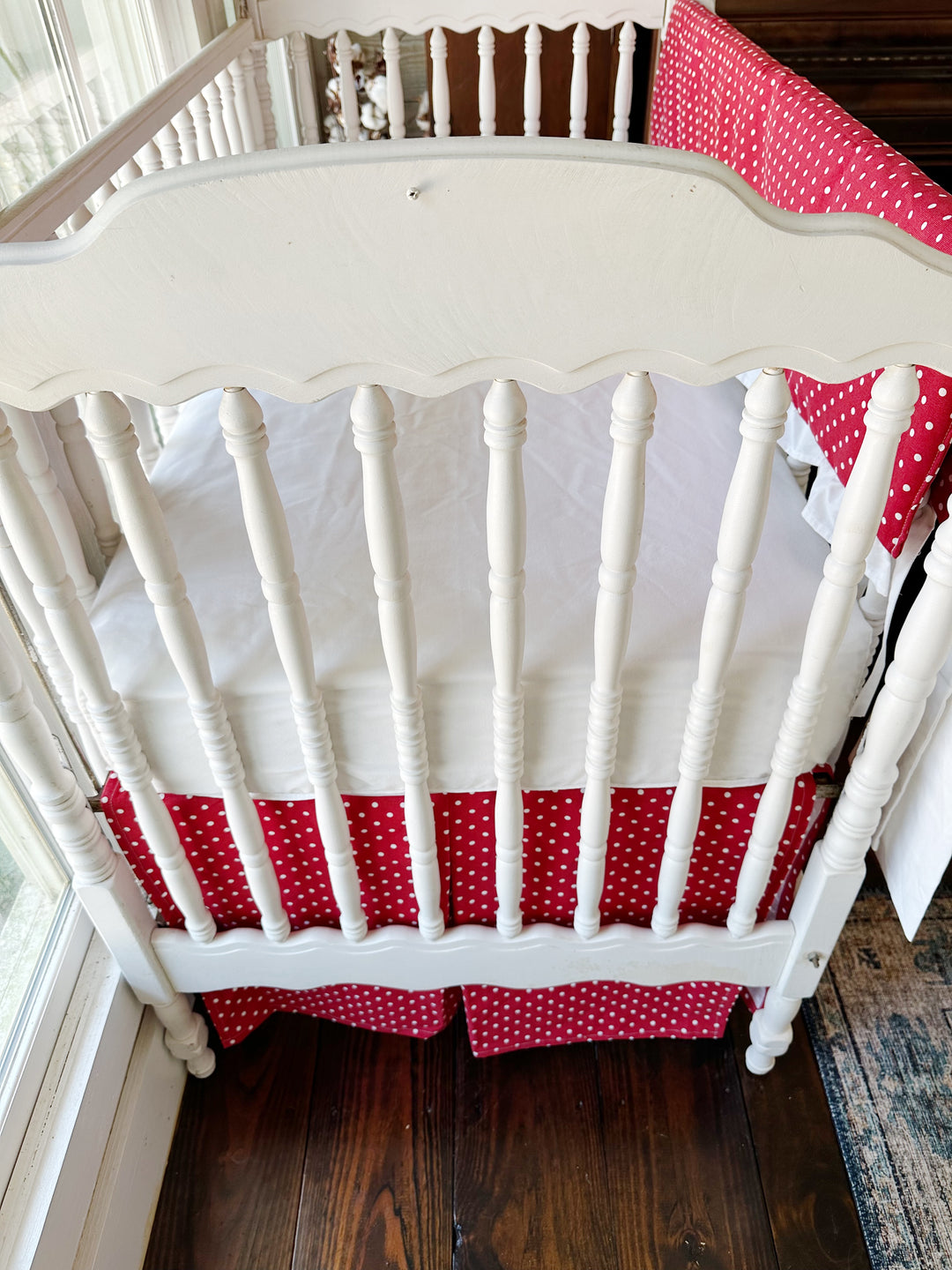 Looking down into the crib at the white sheet above the red polka dot skirt