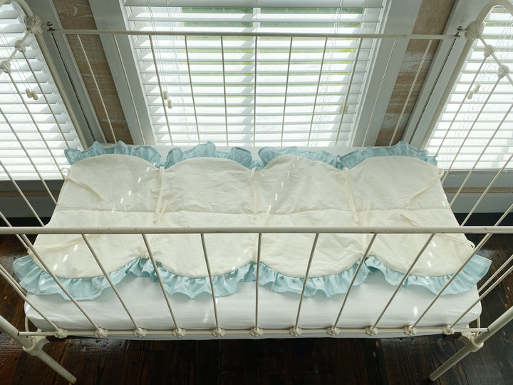 Overhead view of the ivory scalloped crib rail cover showing its full length, mist ruffle and ivory cotton ties