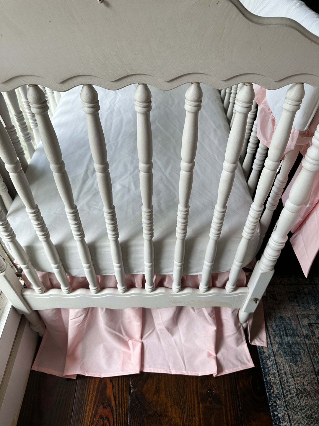 White crib fitted with a Sisters Pink farmhouse crib skirt and white cotton crib sheet in a baby girl nursery