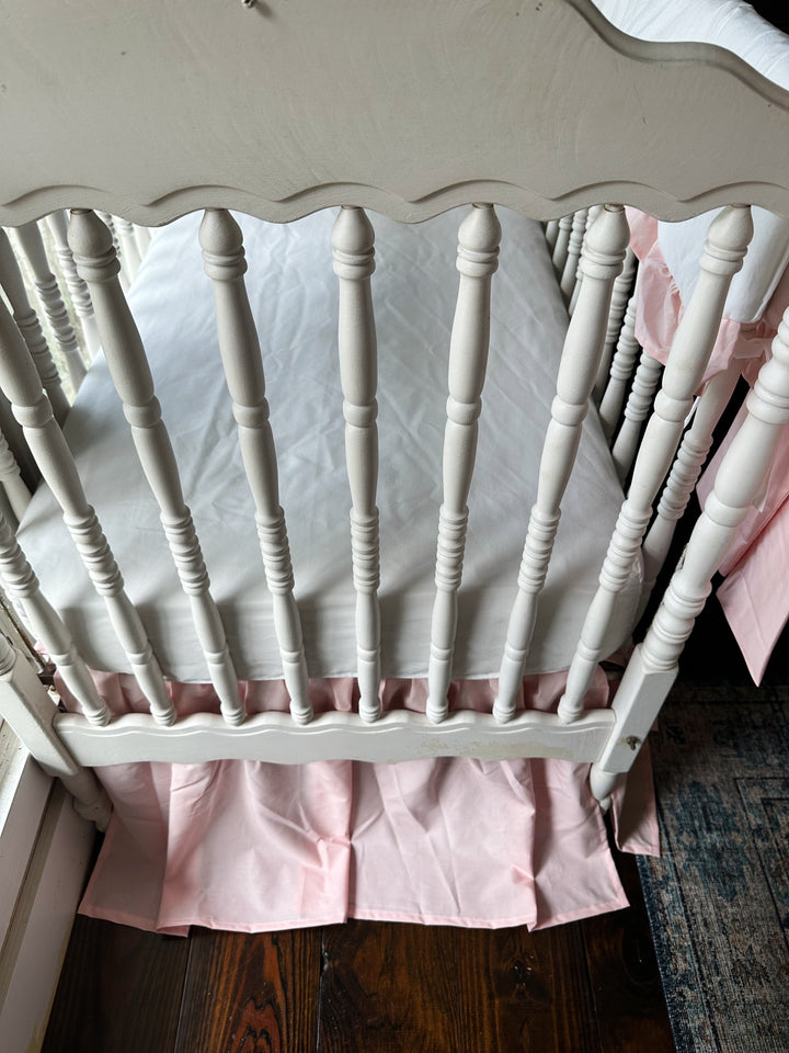 White crib fitted with a Sisters Pink farmhouse crib skirt and white cotton crib sheet in a baby girl nursery