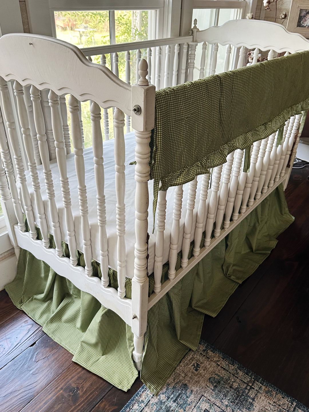 Angled view of pine green gingham crib rail cover and 20 inch four-sided farmhouse crib skirt