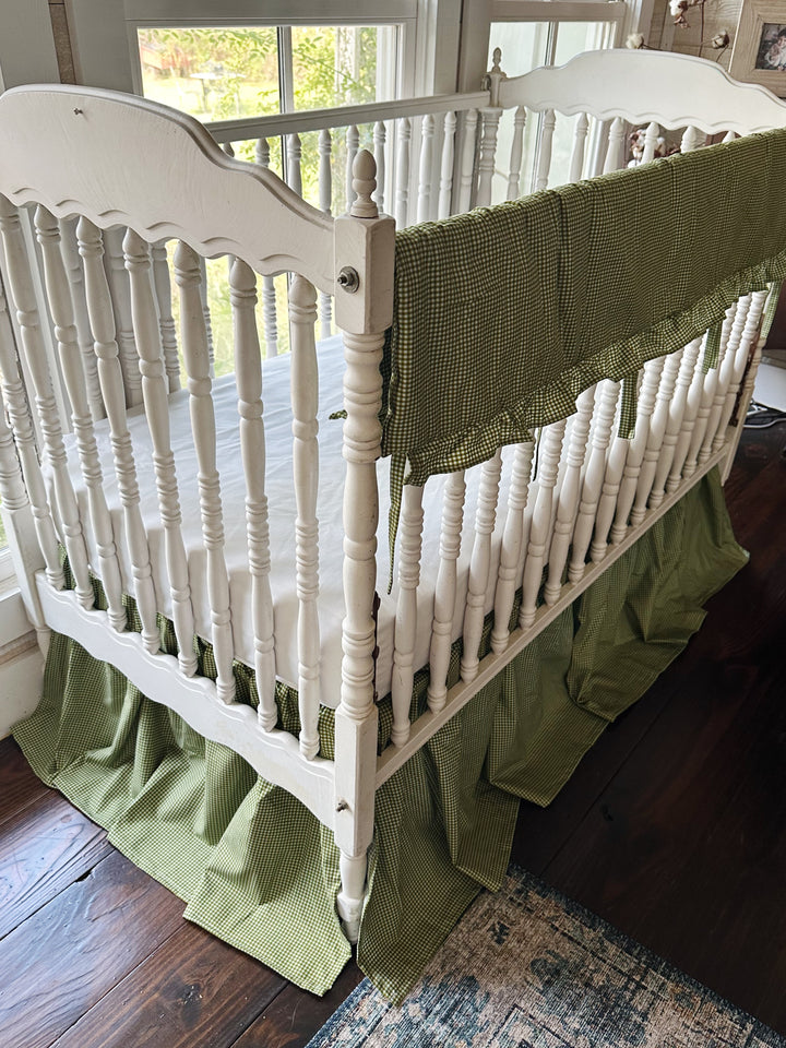 Angled view of pine green gingham crib rail cover and 20 inch four-sided farmhouse crib skirt
