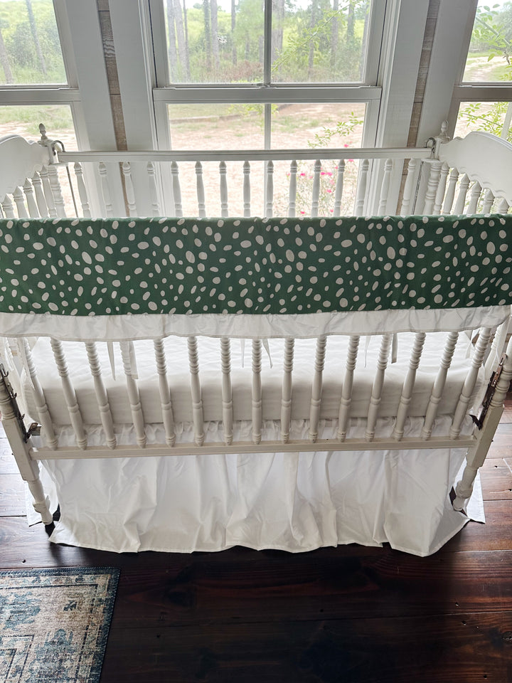 Green and white dot ruffled crib rail cover above a gathered white farmhouse crib skirt, no bows on the posts