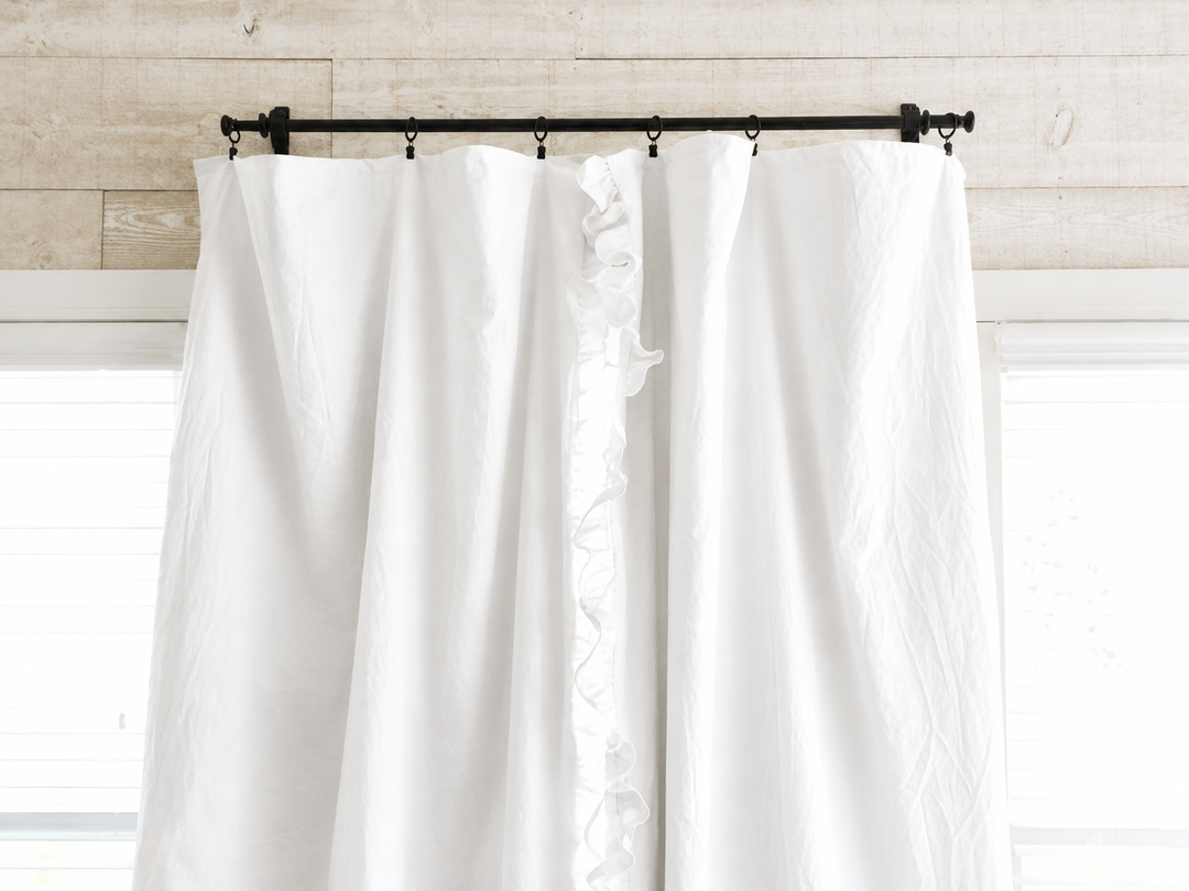 Top of the white curtain panels on a black iron rod with clip rings against whitewashed shiplap - High Cotton Textile