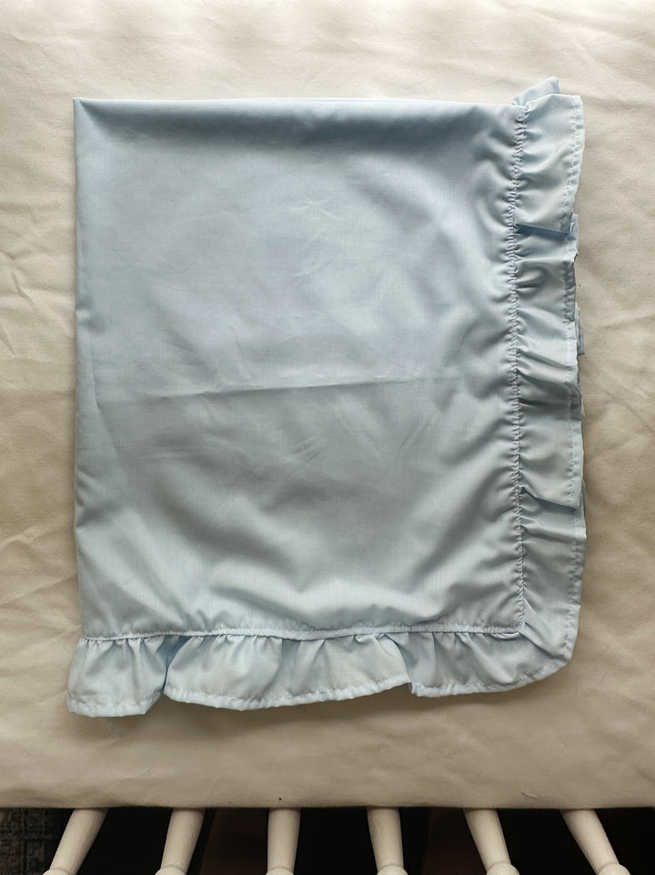 Folded light blue ruffled baby blanket for a baby boy nursery resting on a crib mattress - High Cotton Textile