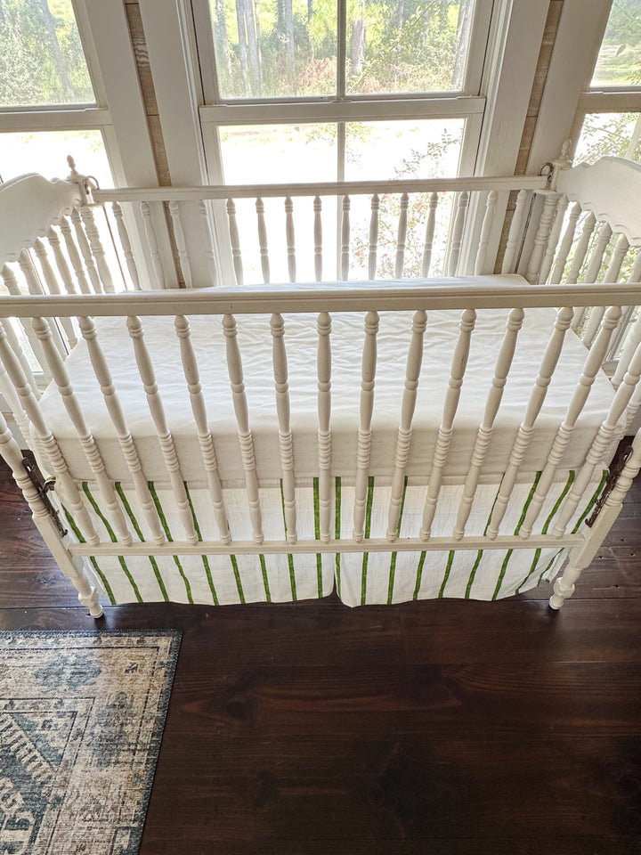 Looking down over the crib rail at the white sheet and the green striped skirt below
