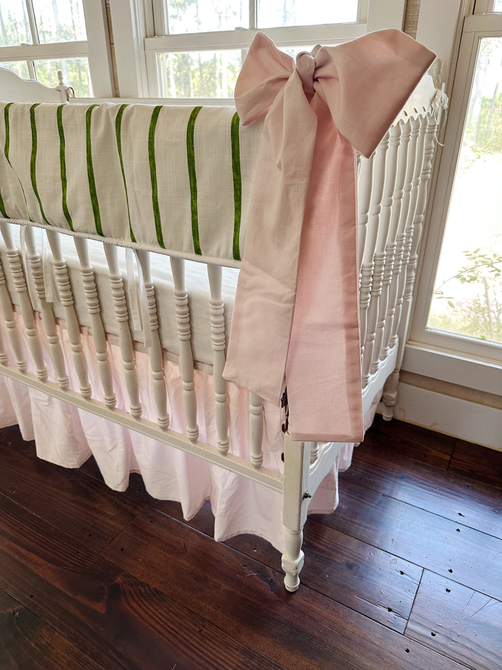 Corner view from the foot of the crib, pink sash hanging the length of the post