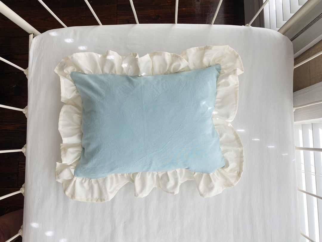 Overhead view of the mist crib pillow and its full ivory ruffle on a crib mattress