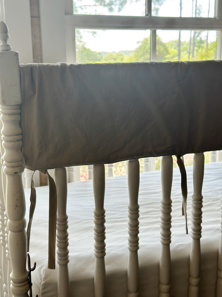 Close-up of oatmeal crib rail cover with fabric ties on white spindle crib rail - High Cotton Textile