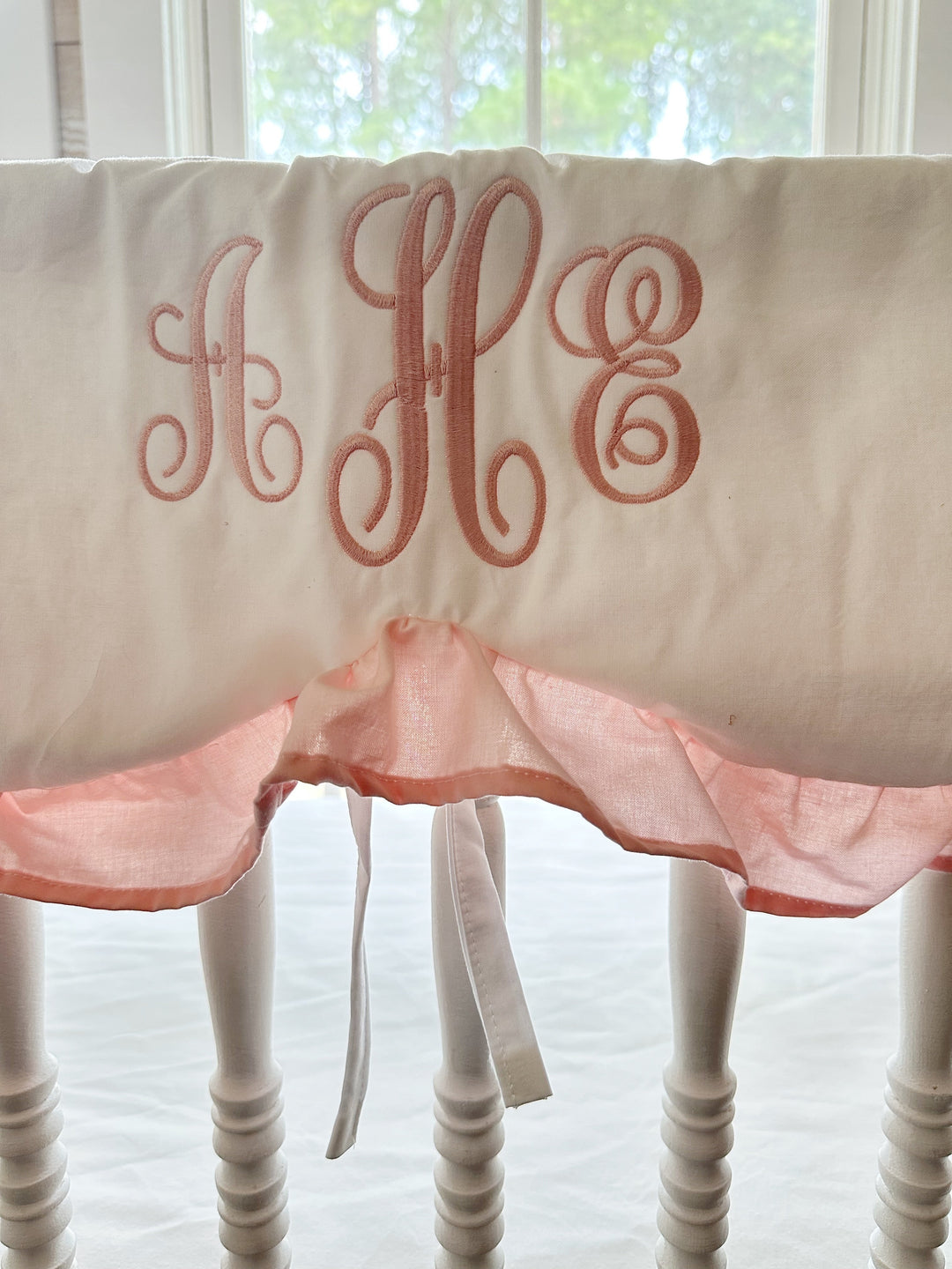 Pink script monogram and Sisters Pink ruffle detail on a white scalloped crib rail cover