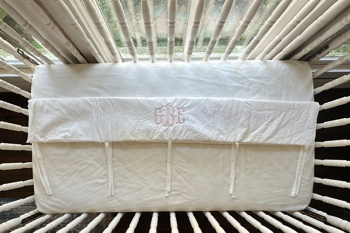 Overhead view of the monogrammed white cover showing the row of narrow cotton ties