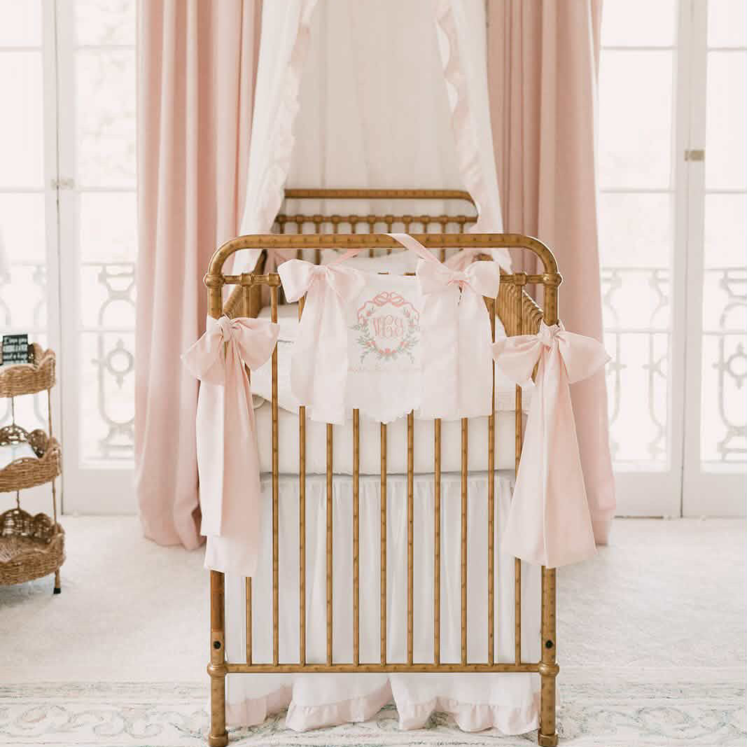 White and baby pink ruffled crib canopy set with crib skirt, monogram pillow and pink bows on gold crib - High Cotton Textile