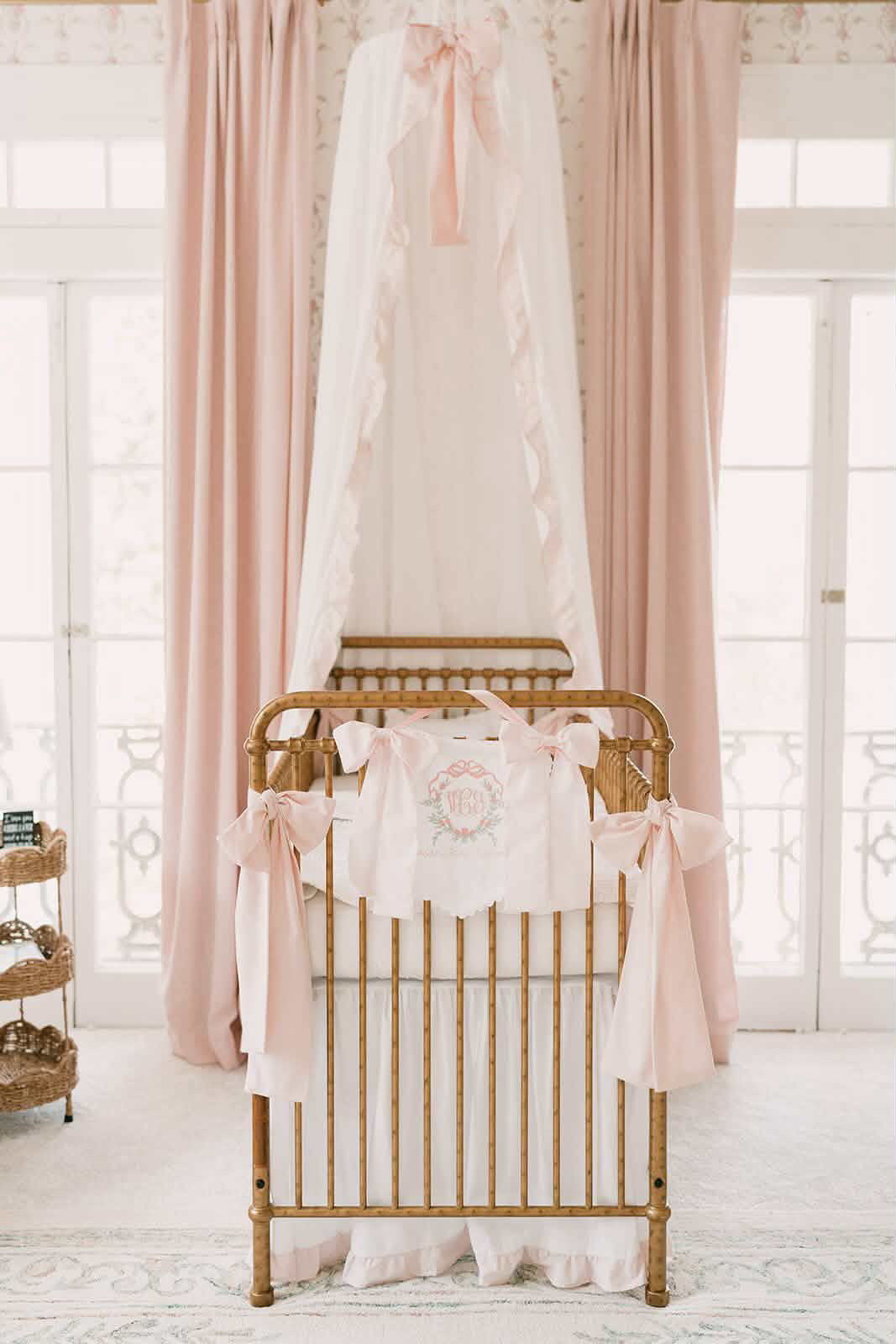 White ruffled crib canopy with baby pink ruffle trim and pink bow on gold crib - High Cotton Textile