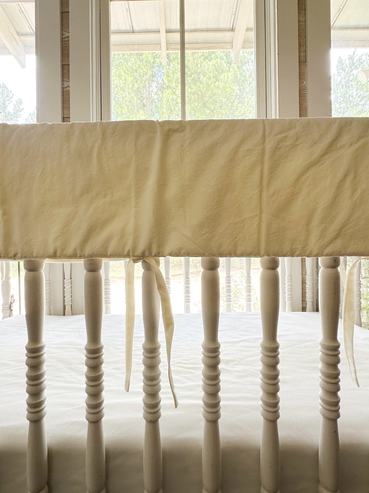 Close view of the ivory cover draped over the crib top rail with ties hanging between spindles