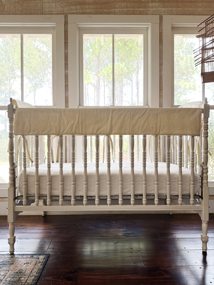 Ivory simple crib rail cover tied across the front top rail of a white spindle crib