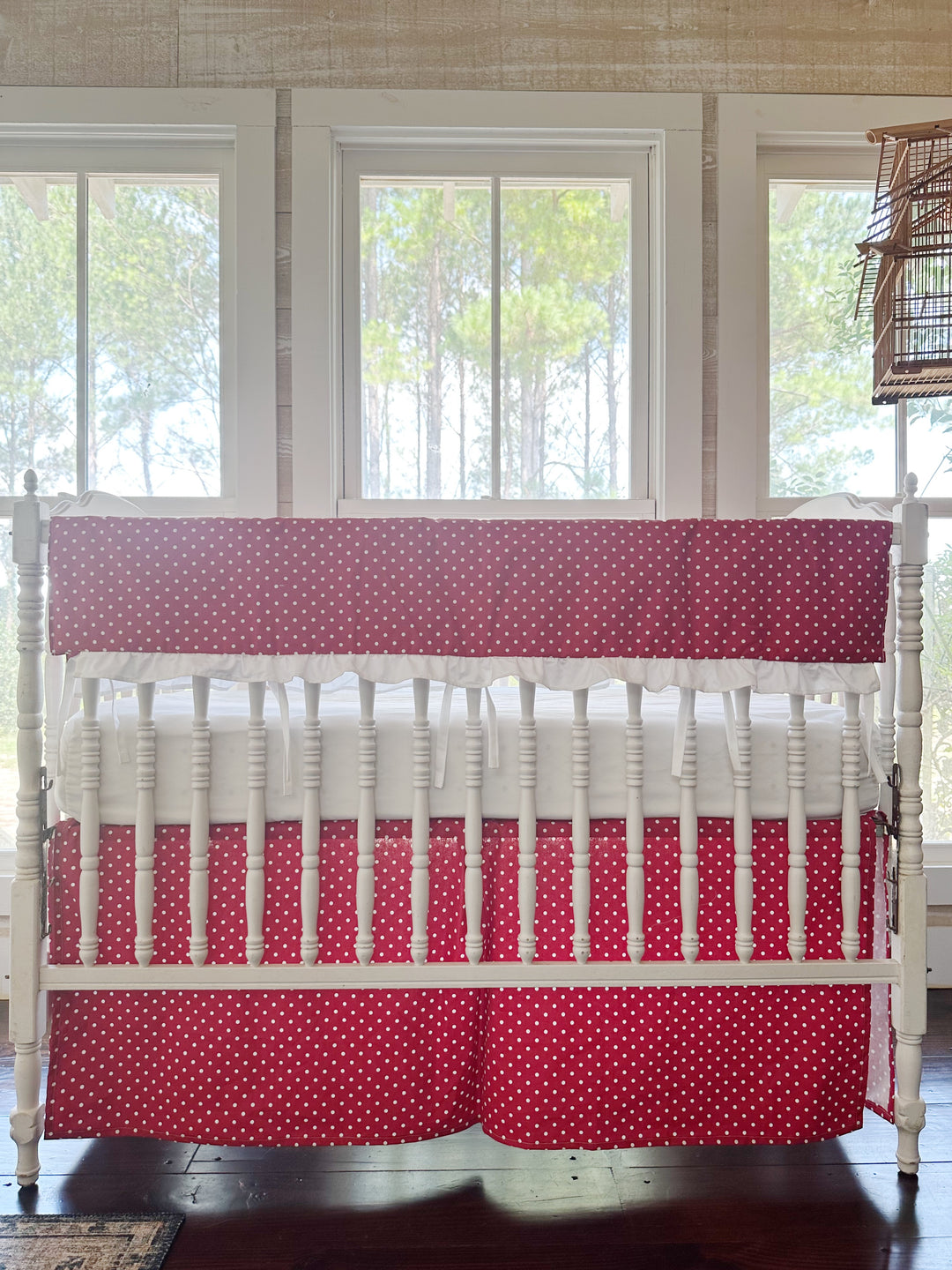 Cherry red and white polka dot ruffled crib rail cover with a matching dotted tailored skirt on a white spindle crib