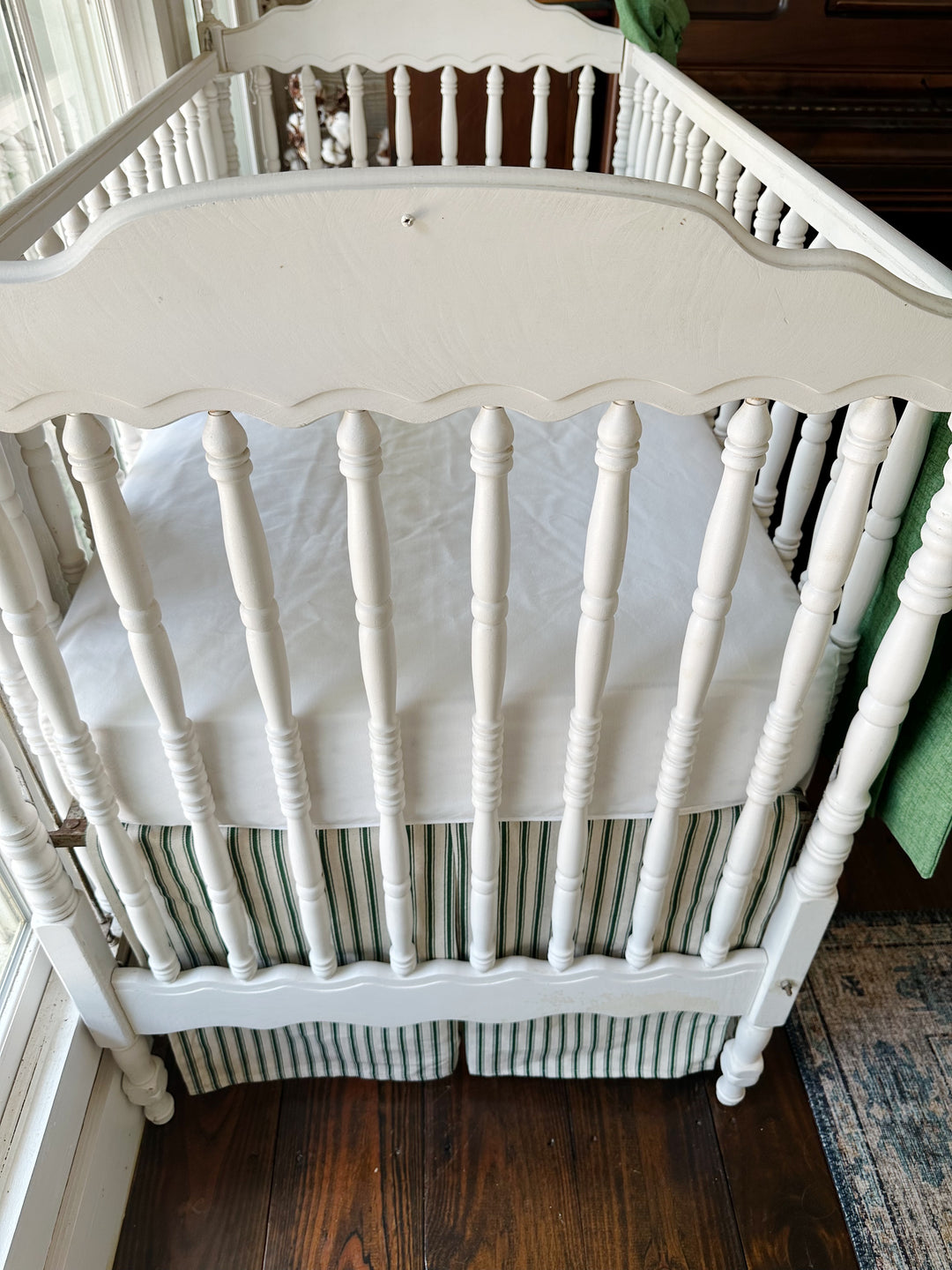 Seen from the end of the crib, the pleated ticking skirt beneath a plain white sheet