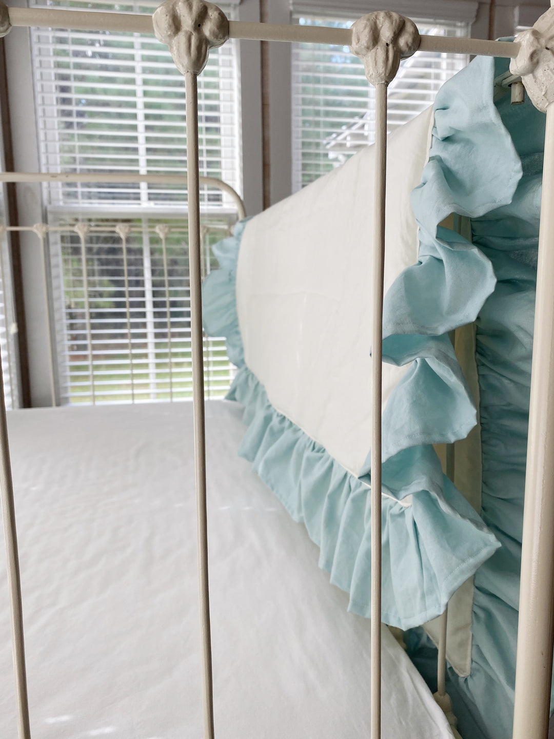 Angled view of the ivory ruffled crib quilt draping over an iron crib in a farmhouse nursery