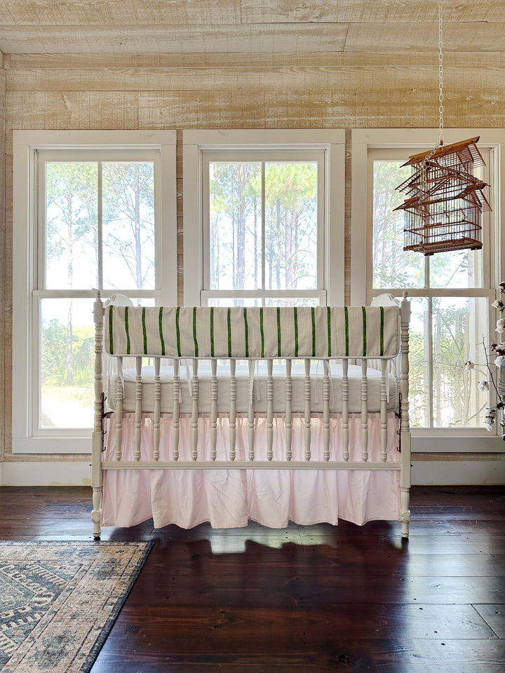 The pink and green crib set in a pine-paneled nursery with three tall windows and a hanging birdcage