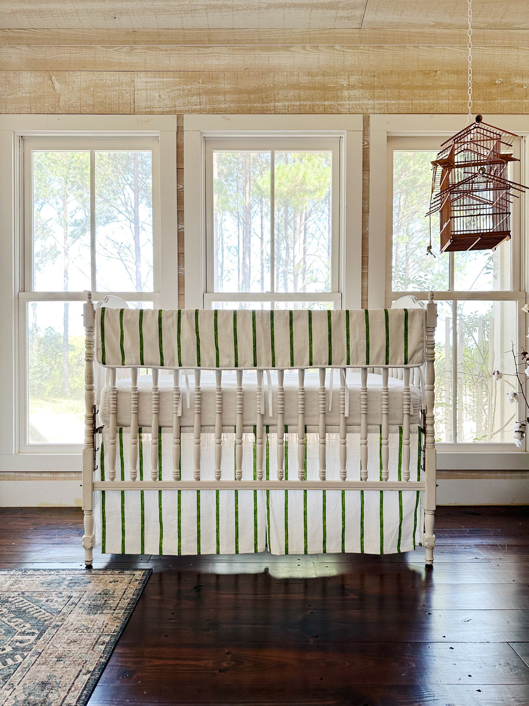 The striped rail cover and skirt seen across a pine-paneled room with three windows and a hanging birdcage