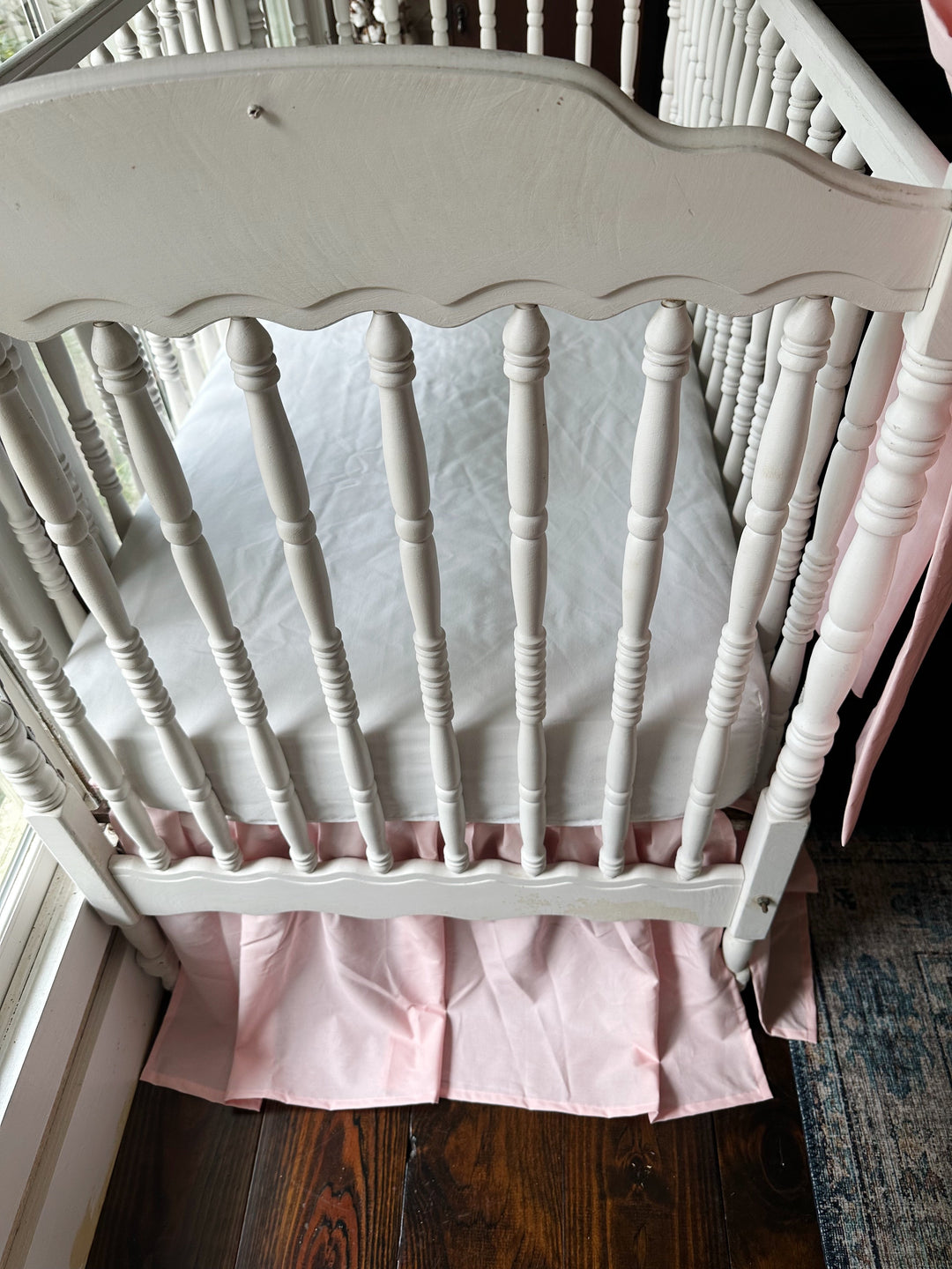 Sisters Pink farmhouse crib skirt seen from above under a white fitted crib sheet