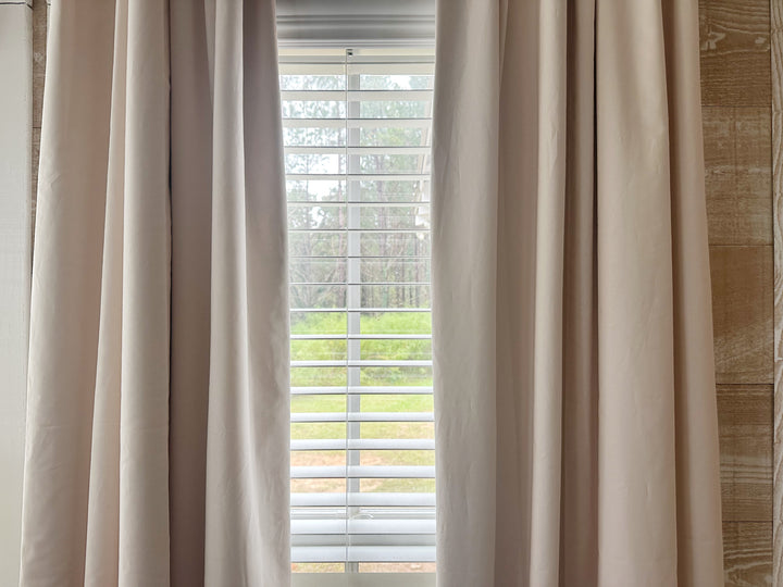 Ballet Slipper Pink panels parted to frame a narrow window with white wood blinds and pine trees outside
