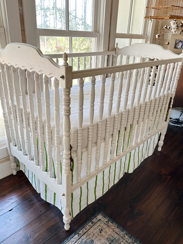 Angled view from the head of the crib, green stripes running straight down the tailored skirt