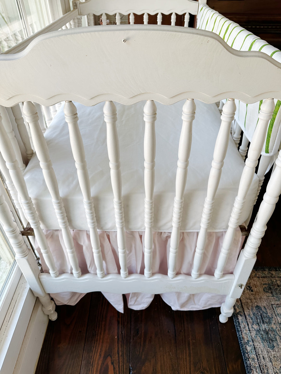 Looking down at the head of the crib, white sheet above the baby pink gathers