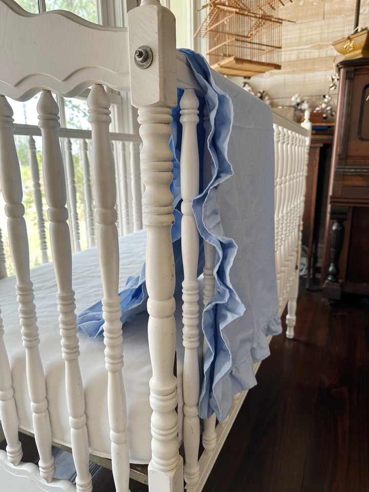 Light blue ruffled baby blanket draped over the end rail of an antique crib, ruffle falling in soft folds - High Cotton Textile