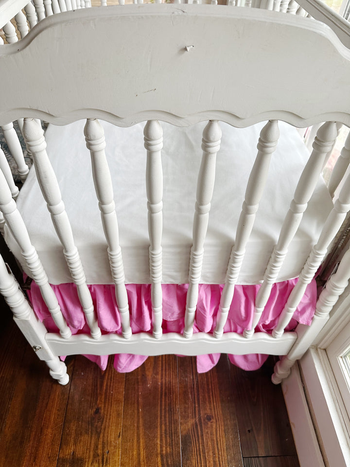 Looking over the scalloped crib end at the white mattress and the parfait pink tiered ruffles below