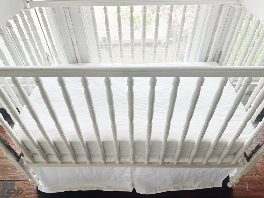 White washed cotton crib skirt viewed from above showing full 4-sided coverage