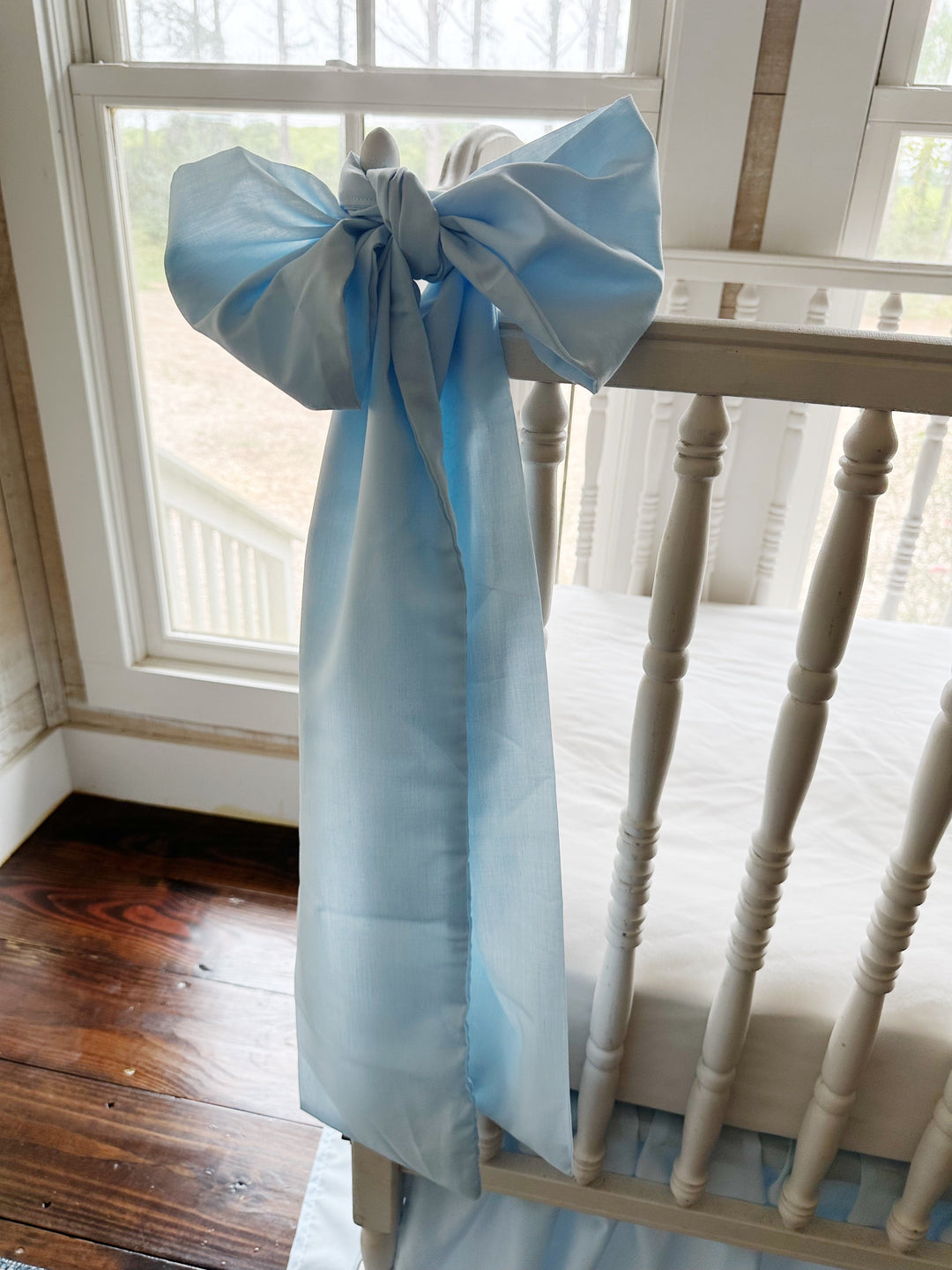 Blue crib bow tied at the corner post with window light coming through the sash