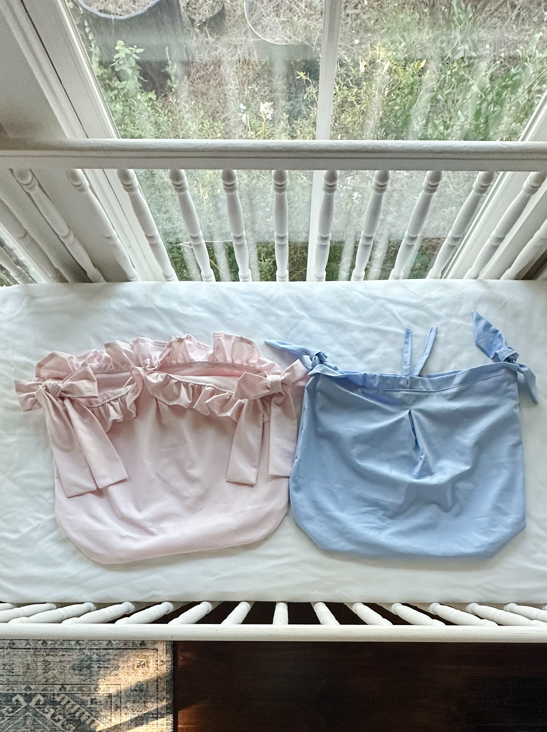 Pink ruffled and blue tailored crib caddies laid flat next to each other on a crib mattress