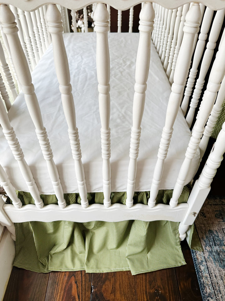 Overhead view of a white fitted crib sheet with the pine green gingham crib skirt