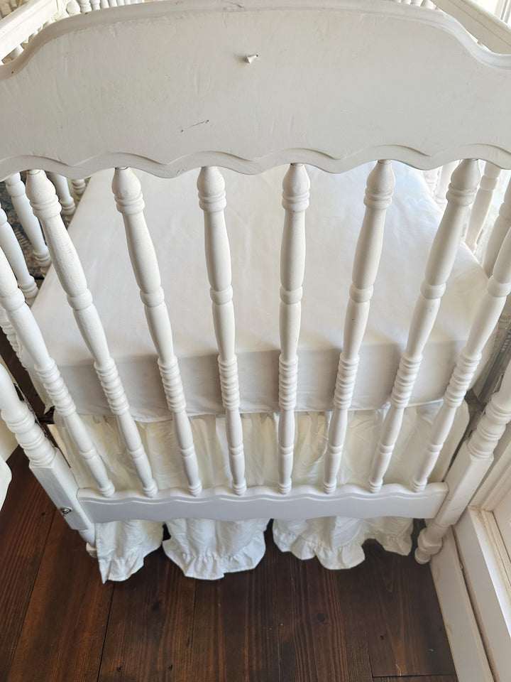 Looking down over the scalloped footboard at the white mattress and the porcelain ruffled skirt beneath
