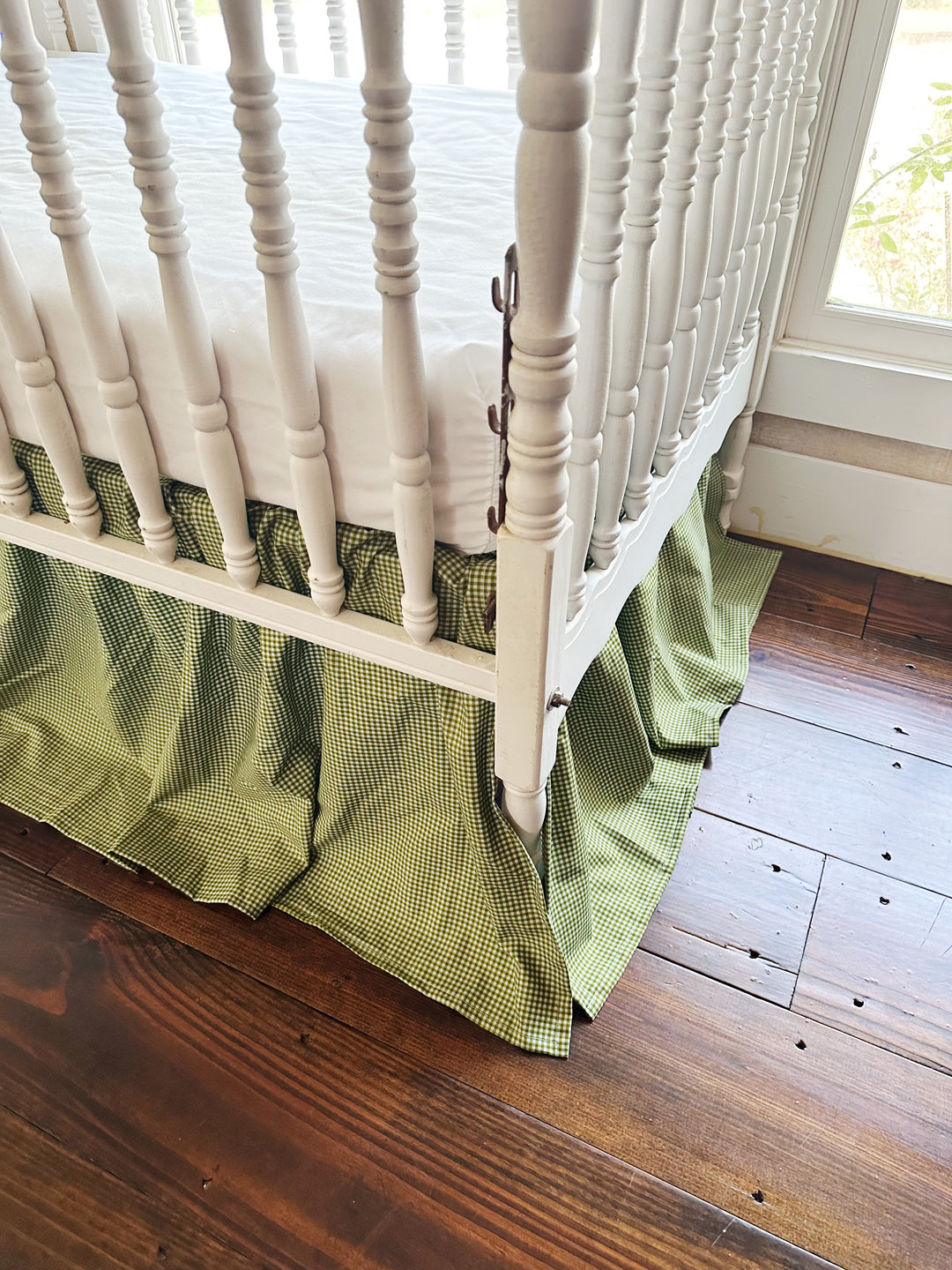 Corner view of the 20 inch pine green gingham crib skirt reaching toward a wood floor