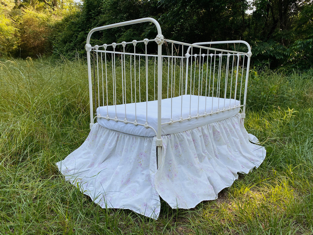Handmade lavender floral gathered crib skirt on white iron crib in open field