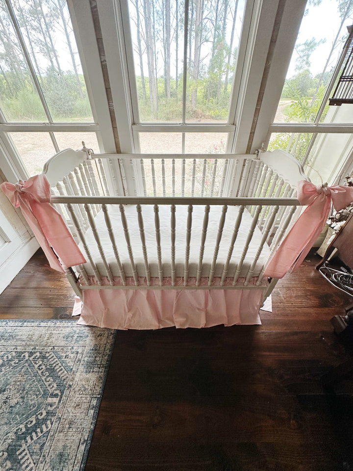 Overhead view of a Sisters Pink gathered crib skirt with two pink bow sashes tied to the crib corner posts