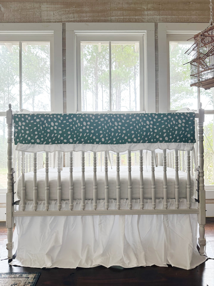 Straight-on view of the two-piece green dot crib set with the white ties hanging between the spindles