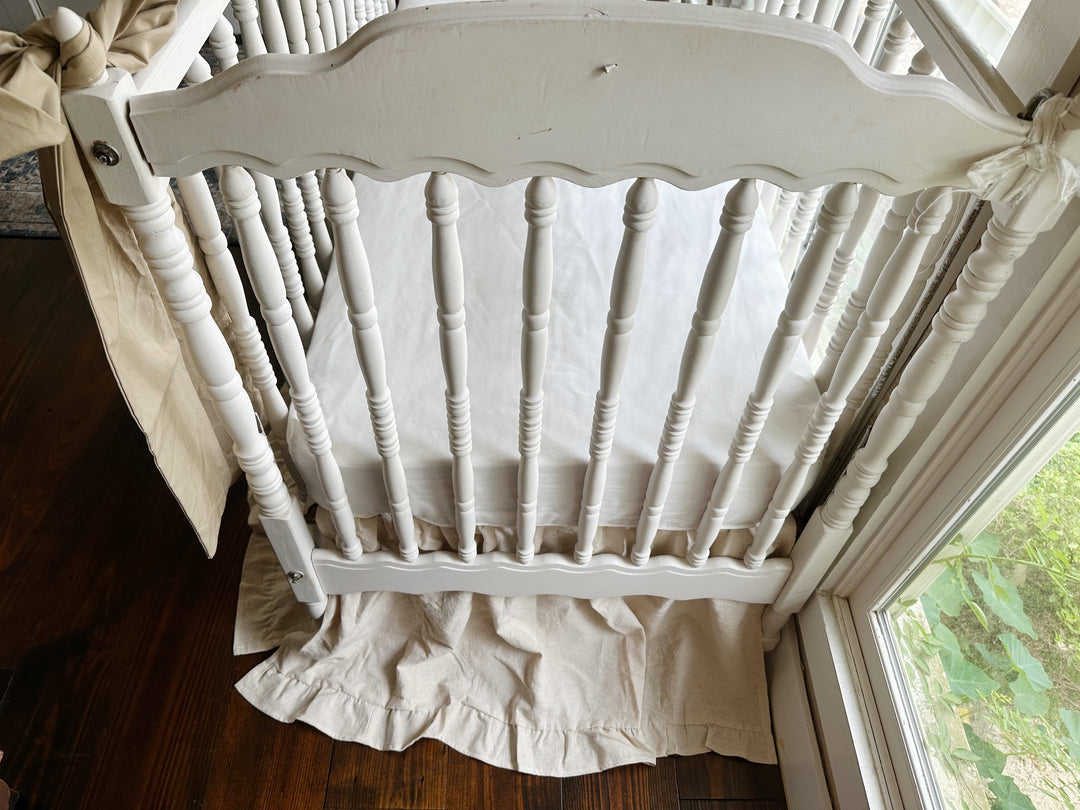 Neutral ruffled crib skirt in natural osnaburg with two large oatmeal crib bows on a white crib - High Cotton Textile